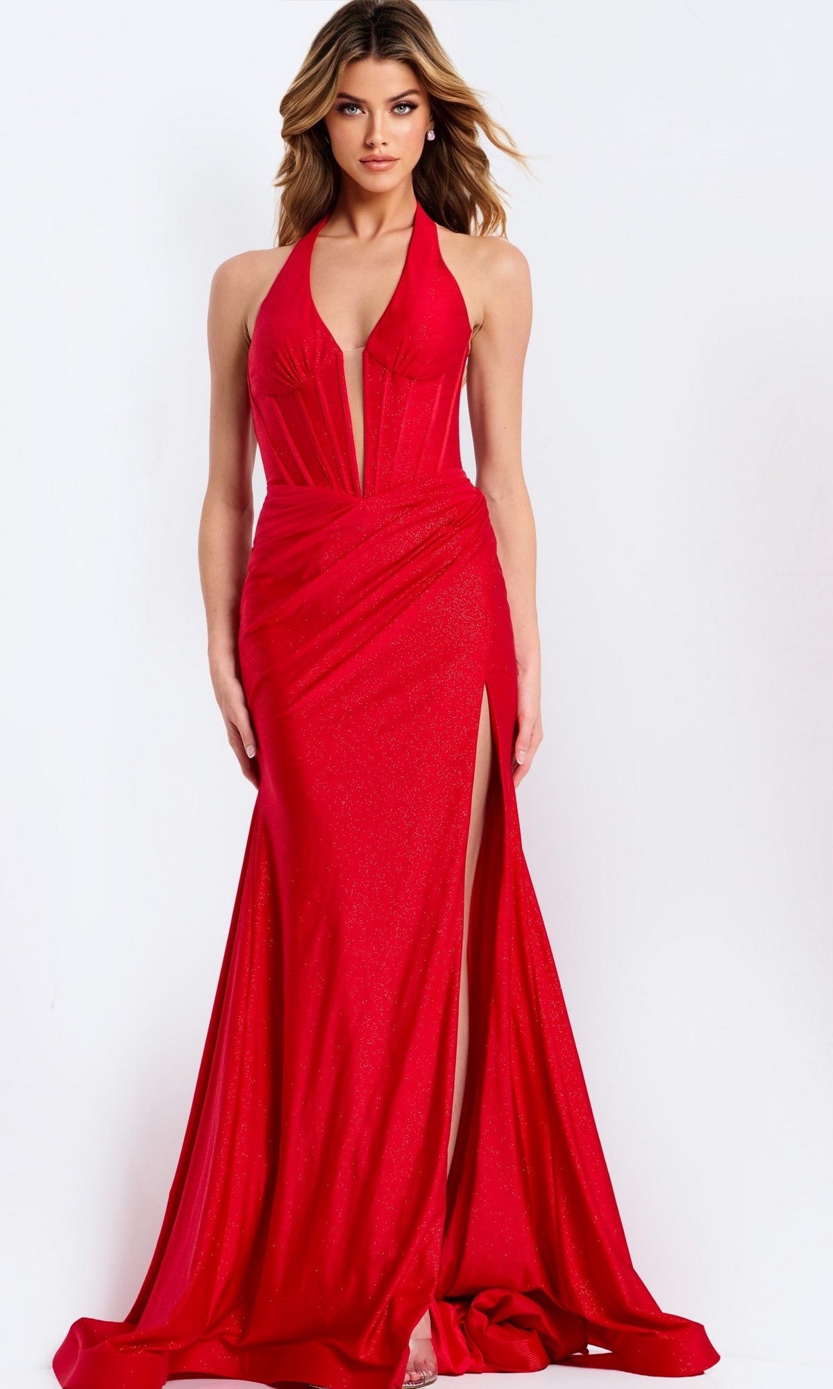 A woman stands against a plain white background wearing the Jovani 46489 long red prom dress, which features a halter neckline, sheer bodice, plunging v-neckline, and a dramatic high-leg side slit.